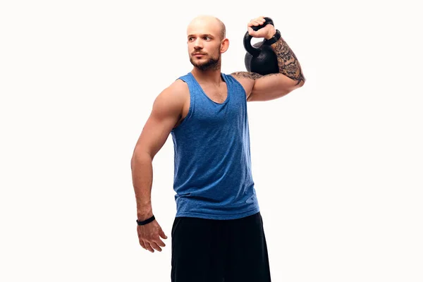 Sportovní vyholenou hlavou muž s tetováním na ruce drží kettlebell. — Stock fotografie