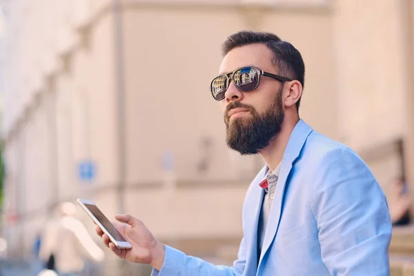 Skäggig man i solglasögon med en smartphone — Stockfoto