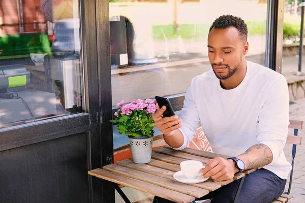 Мужчина пьет кофе и пользуется смартфоном — стоковое фото