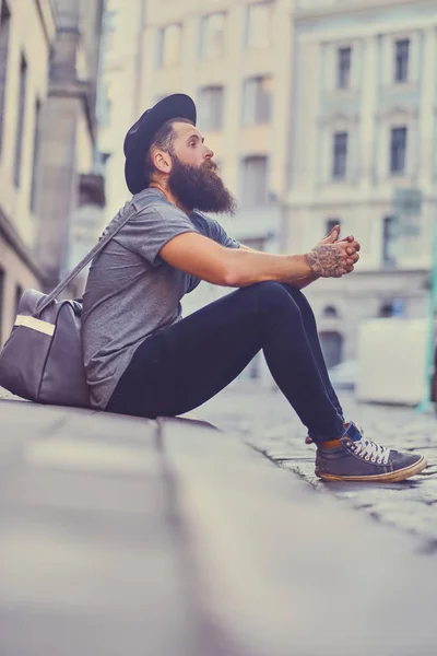 Bearded hipster sits on a step on a street — Stock Photo, Image