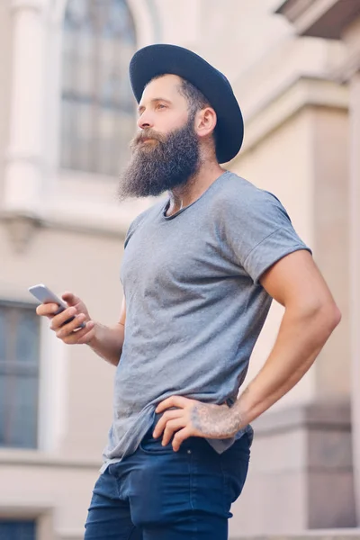 Varón barbudo con sombrero sostiene un smartphone . —  Fotos de Stock