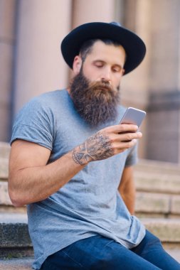 Sakallı erkek şapkalı bir akıllı telefon tutar.