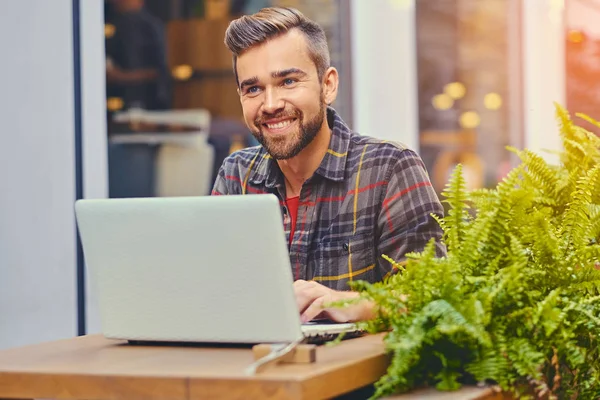 Szakállas férfi használ egy laptop egy kávézóban — Stock Fotó