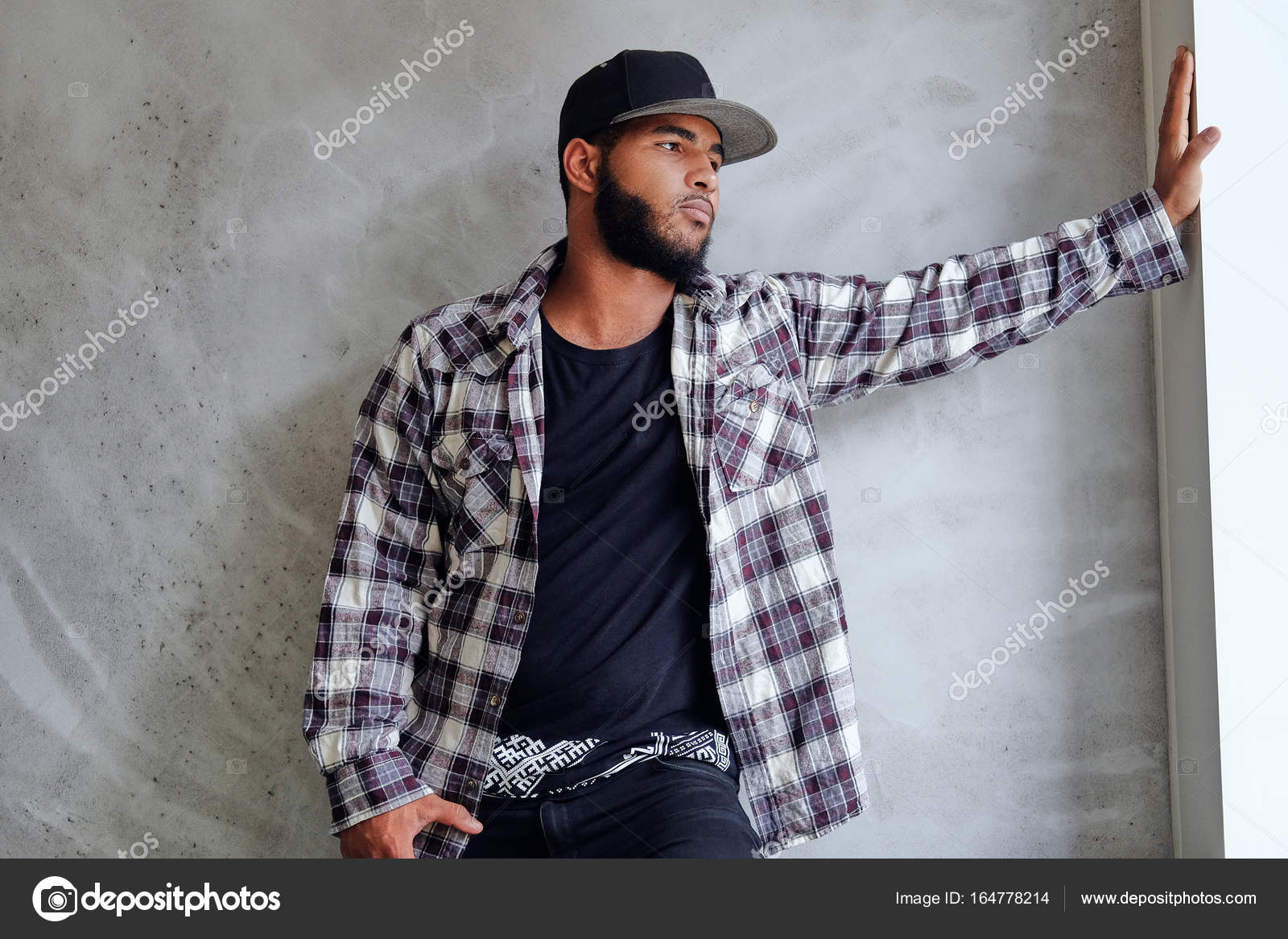 Hipster noir, barbu mâle vêtu d\u0027une chemise de laine et un bonnet, posant près de fenêtre avec lumière naturelle \u2014 Image de fxquadro