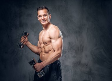 Gömleksiz adam dumbbells bir kümesini tutar.