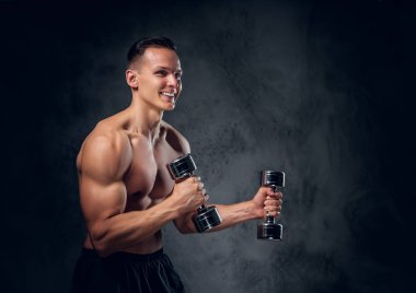Gömleksiz adam dumbbells bir kümesini tutar.