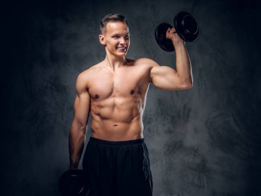 Gömleksiz adam dumbbells bir kümesini tutar.