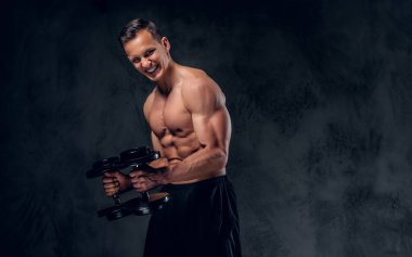 Gömleksiz adam dumbbells bir kümesini tutar.