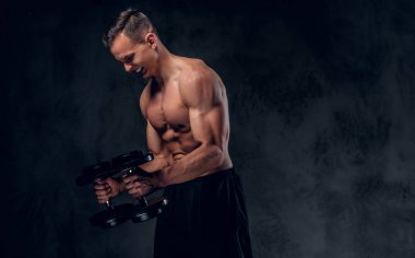 Gömleksiz adam dumbbells bir kümesini tutar.