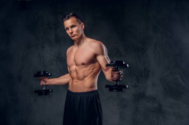Gömleksiz adam dumbbells bir kümesini tutar.