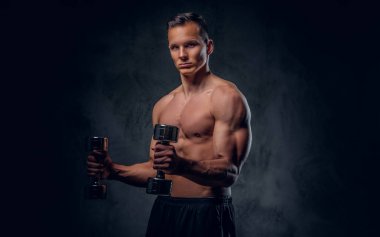 Gömleksiz adam dumbbells bir kümesini tutar.