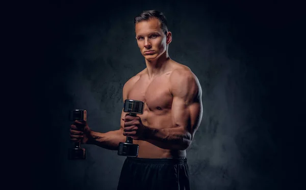 Homem sem camisa segura um conjunto de halteres . — Fotografia de Stock