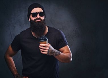 Kahve fincanı sakallı dövmeli adam tutar.