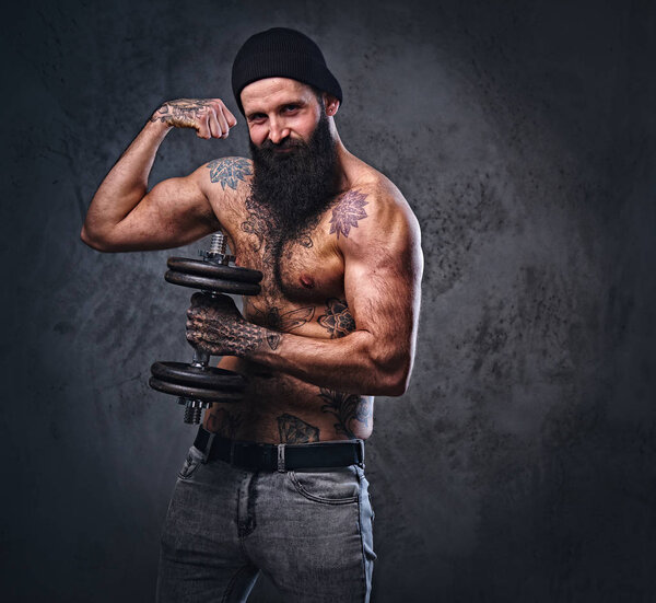 Shirtless bearded male holds dumbbell.