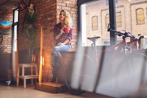 Sarışın kadın pencerenin sıcak kahve içer.