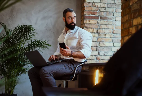 Hombre barbudo urbano usando un portátil en una habitación . — Foto de Stock