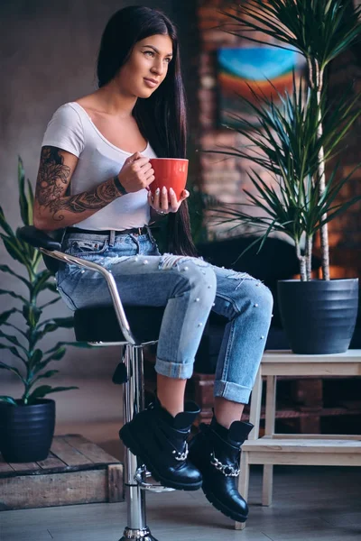 Tattooed brunette female drinks coffee