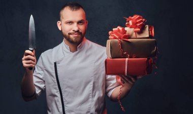 Sakallı şef aşçı portre renkli kağıt Noel hediyeleri gri arka plan üzerinde tutar..