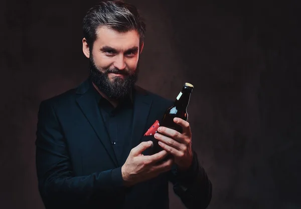 A stylish bearded male dressed in a black suit presenting craft beer.