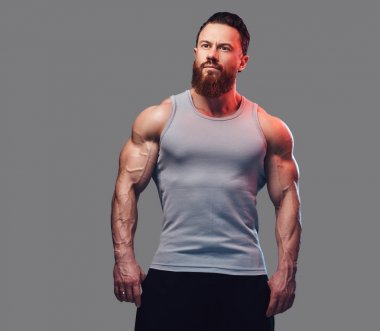 Gri arka plan üzerinde izole bir kolsuz gömlek giymiş acımasız sakallı vücut geliştirmeci portresi.