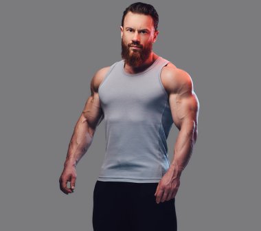 Gri arka plan üzerinde izole bir kolsuz gömlek giymiş acımasız sakallı vücut geliştirmeci portresi.