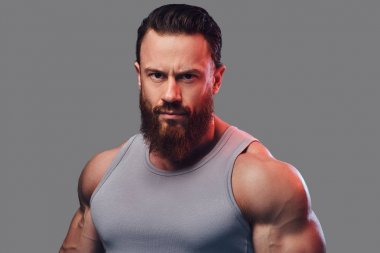 Gri arka plan üzerinde izole bir kolsuz gömlek giymiş acımasız sakallı vücut geliştirmeci portresi.