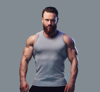 Gri arka plan üzerinde izole bir kolsuz gömlek giymiş acımasız sakallı vücut geliştirmeci portresi.
