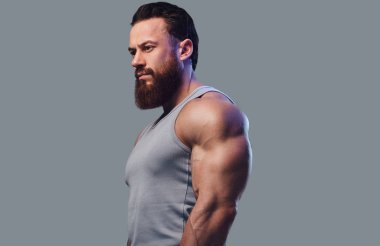 Gri arka plan üzerinde izole bir kolsuz gömlek giymiş acımasız sakallı vücut geliştirmeci portresi.