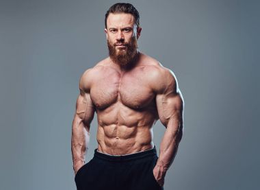 Sakallı gömleksiz vücut geliştirmeci gri arka plan üzerinde portresi.