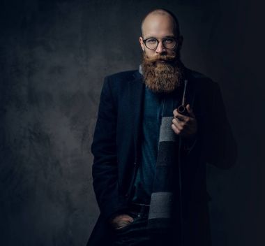 Kızıl saçlı sakallı erkek takım elbise ve gelenek pipo koyu gri arka plan üzerinde gözlük giyinmiş.