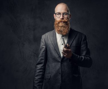 Kızıl saçlı sakallı erkek takım elbise ve gelenek pipo koyu gri arka plan üzerinde gözlük giyinmiş.