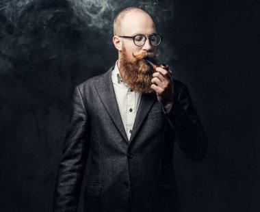 Kızıl saçlı sakallı erkek takım elbise ve gelenek pipo koyu gri arka plan üzerinde gözlük giyinmiş.