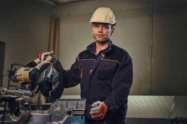 Sarı kap testere bir garajda çalışır bir emanet marangoz erkek giymiş.