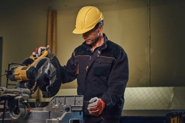 Sarı kap testere bir garajda çalışır bir emanet marangoz erkek giymiş.