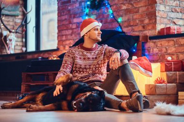 Sakallı hippi erkek çekici ile onun Rottweiler köpek Noel dekorasyonu ile bir odada bir katta oturur.