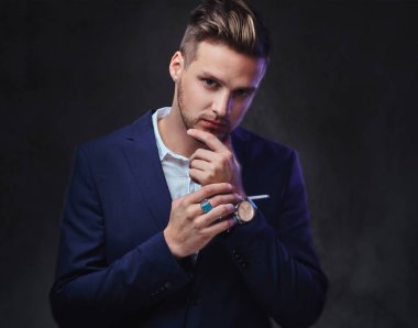 Koyu gri arka plan üzerinde bir takım elbise giymiş bir çekici sarışın erkek.