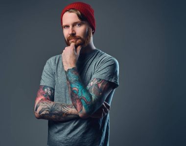 Kızıl saçlı sakallı erkek gri arka plan üzerinde poz kollarını dövmeler ile.