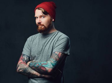 Kızıl saçlı sakallı erkek gri arka plan üzerinde poz kollarını dövmeler ile.