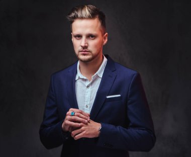 Koyu gri arka plan üzerinde bir takım elbise giymiş bir çekici sarışın erkek.