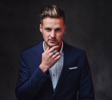 Koyu gri arka plan üzerinde bir takım elbise giymiş bir çekici sarışın erkek.