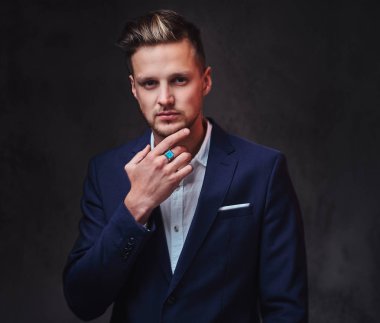 Koyu gri arka plan üzerinde bir takım elbise giymiş bir çekici sarışın erkek.