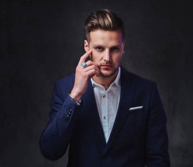 Koyu gri arka plan üzerinde bir takım elbise giymiş bir çekici sarışın erkek.