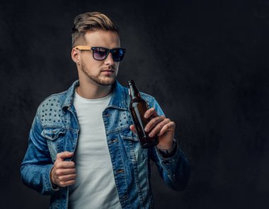 Pozitif sarışın erkek denim ceket ve güneş gözlüğü giymiş bir zanaat bira şişesiyle tutar.