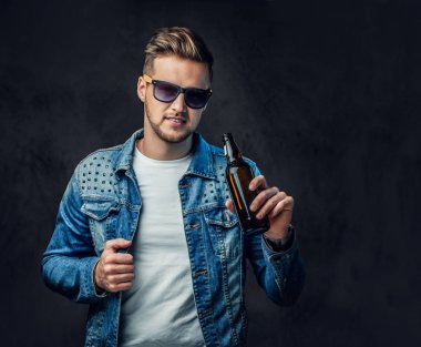 Pozitif sarışın erkek denim ceket ve güneş gözlüğü giymiş bir zanaat bira şişesiyle tutar.