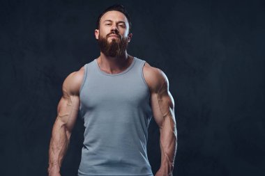 Gri arka plan üzerinde izole bir kolsuz gömlek giymiş acımasız sakallı vücut geliştirmeci portresi.