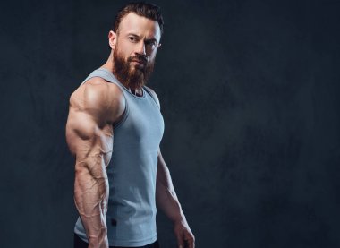 Gri arka plan üzerinde izole bir kolsuz gömlek giymiş acımasız sakallı vücut geliştirmeci portresi.
