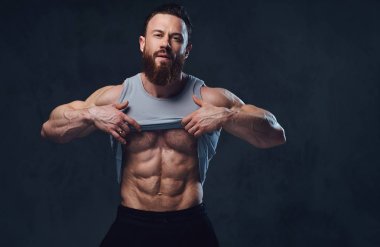Gri arka plan üzerinde izole bir kolsuz gömlek giymiş acımasız sakallı vücut geliştirmeci portresi.