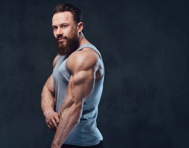 Gri arka plan üzerinde izole bir kolsuz gömlek giymiş acımasız sakallı vücut geliştirmeci portresi.