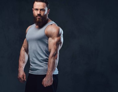 Gri arka plan üzerinde izole bir kolsuz gömlek giymiş acımasız sakallı vücut geliştirmeci portresi.
