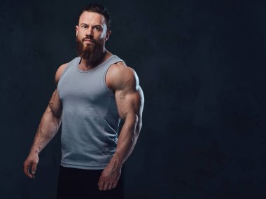 Gri arka plan üzerinde izole bir kolsuz gömlek giymiş acımasız sakallı vücut geliştirmeci portresi.